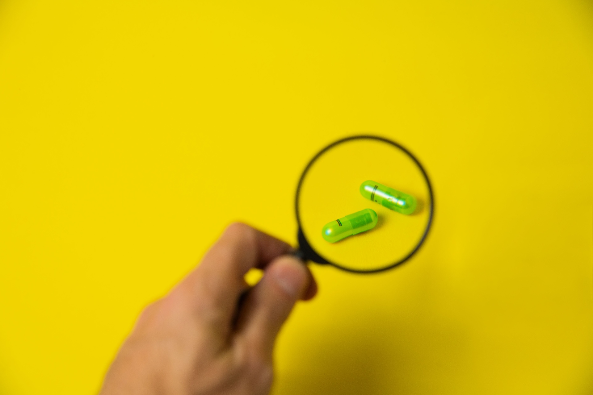 Magnifying glass inspecting green supplement capsules — batch traceability and quality control